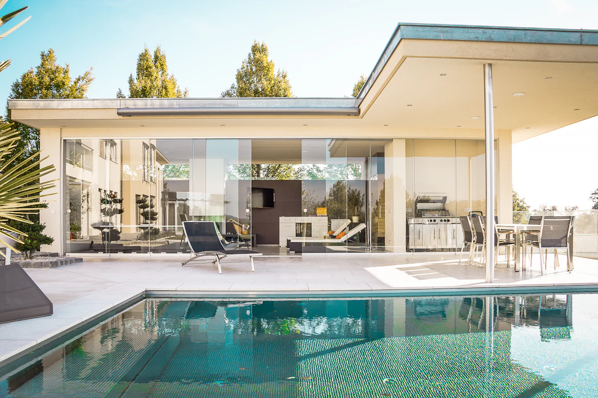 A single-story home with floor-to-ceiling glass walls opening onto a pool deck
