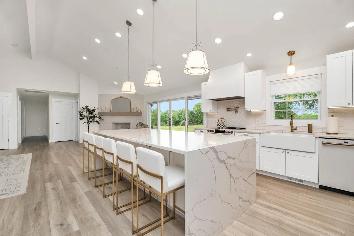 A bright kitchen with a long marble island, pendant lights and white cabinetry